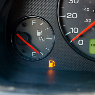 A gas guage in a car reads empty and shows the warning light to let the driver know they are out of gas and need to refuel.